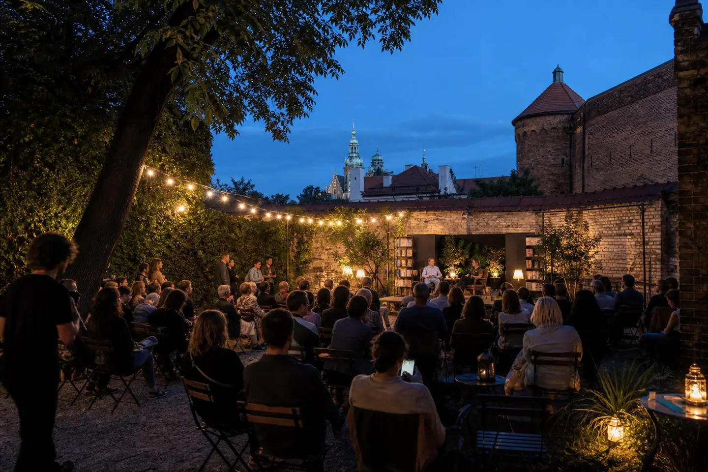 Visitors gathered for an early-evening cultural event in a leafy historic Krakow courtyard